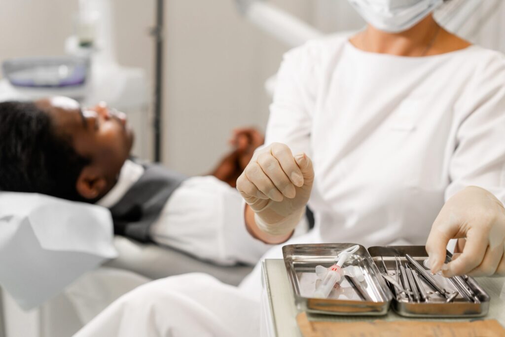 Dental instruments in the foreground. Woman dentist treating root canals in the dental clinic. Man patient lying on dentist chair with open mouth.