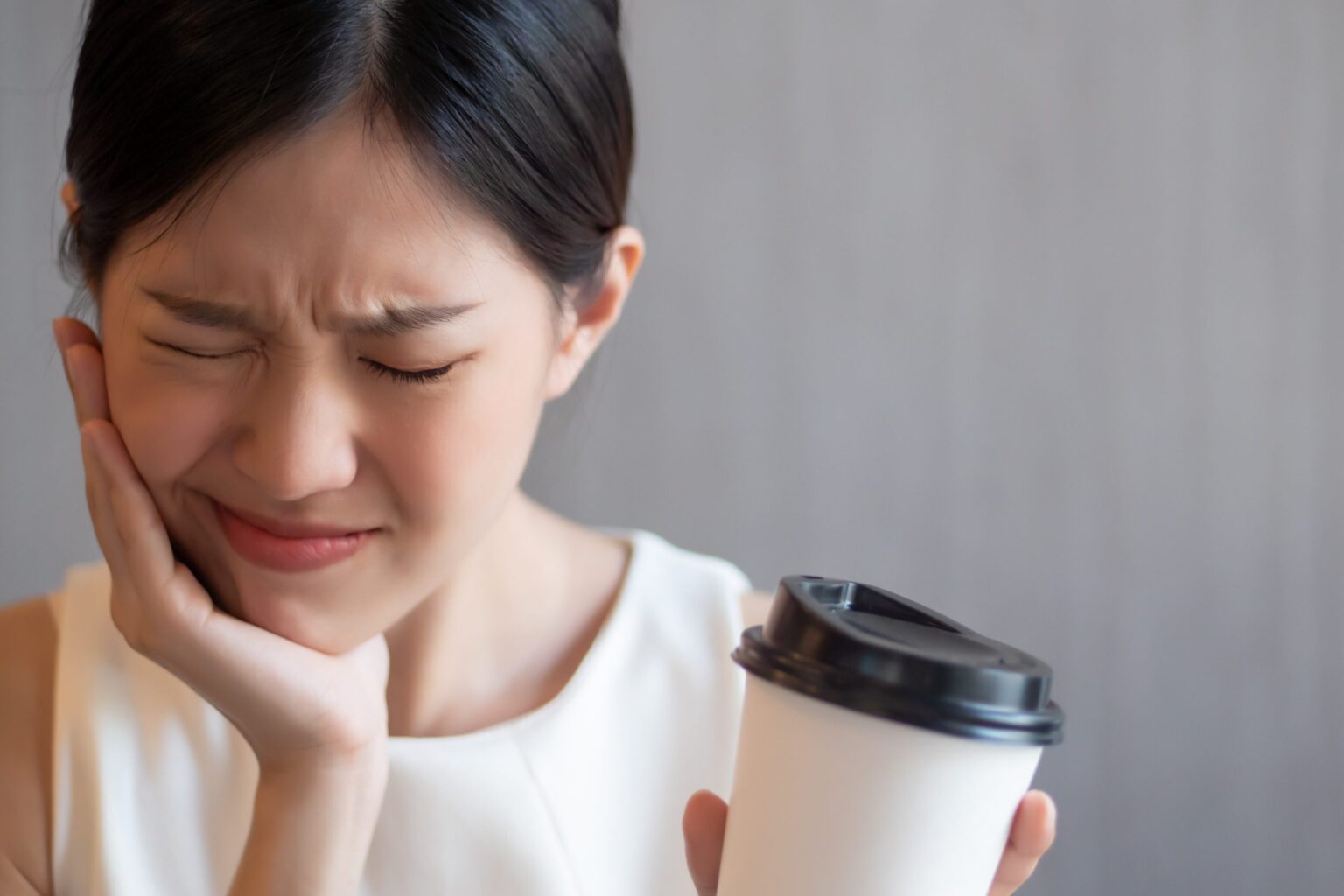 Asian woman grabbed her cheek because of strong tooth pain, holding a coffe cup in her hand