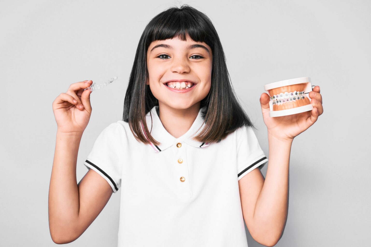 Young little girl with bang holding invisible aligner orthodontic and braces smiling with a happy and cool smile on face, showing teeth.