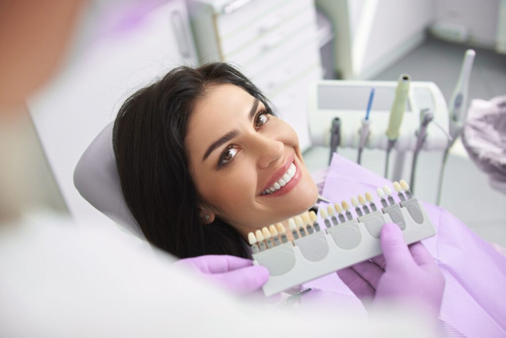 Smiling lady choosing crown color from palette at dental clinic