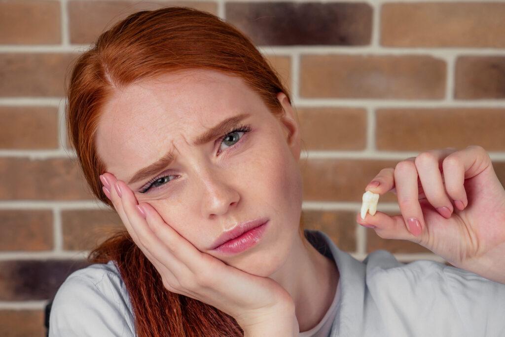 Sad ginger heared woman holding extracted tooth with her fingers